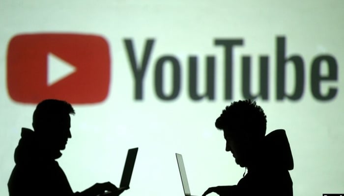 A representational image of toy men using laptops silhouetted against a screen lit up with Youtubes logo. — Reuters