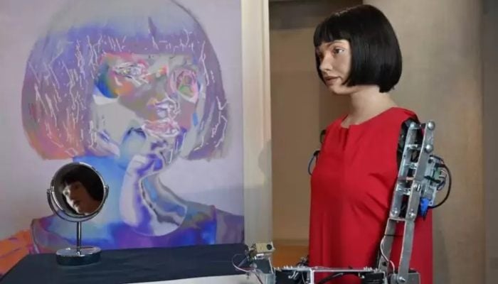 The worlds first ultra-realistic AI robot artist, Ai-Da, who can draw, paint and is a performance artist, is pictured alongside her self-portrait during a press preview of the exhibition Ai-Da: Portrait of the Robot at the Design Museum in London, on May 14, 2021. — AFP
