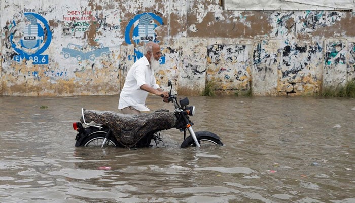 A man pushes his bike as he wades through a flooded road during the monsoon season in Karachi. — Reuters/File