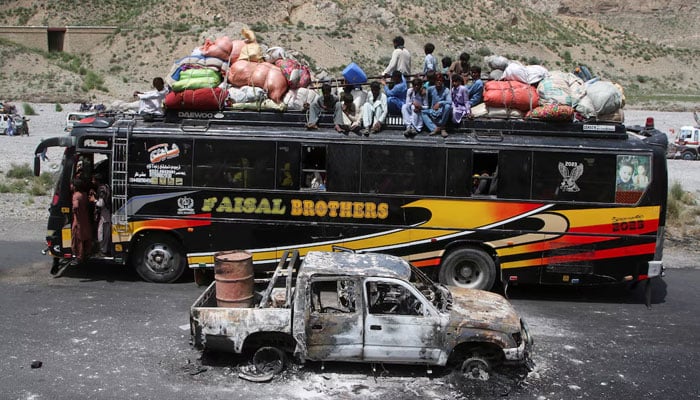 A bus with passengers sitting on the roof with belongings, drives past a damaged vehicle, a day after militants conducted deadly attacks, in Bolan district of Balochistan, August 27, 2024. — Reuters