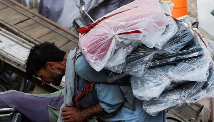 A labourer bends over as he carries packs of textile fabric on his back to deliver to a nearby shop in a market in Karachi. — Reuters/File