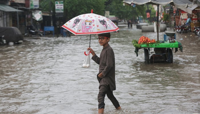 A Child holds an umbrella as he wades through a flooded street after a downpour in Lahore, July 9, 2025. — Reuters