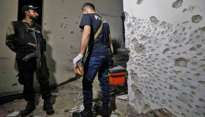 A member of the forensic team walks past a police officer amid the damage in the aftermath of an attack on a police station in Karachi on February 17, 2023. — Reuters
