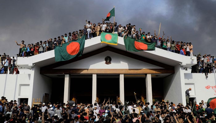 Anti-government protesters display Bangladesh´s national flag as they storm Prime Minister Sheikh Hasinas palace in Dhaka on August 5, 2024. — AFP