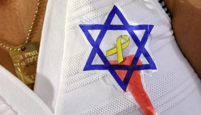 A demonstrator poses with a yellow ribbon pinned to her chest atop a paper drawing depicting a Star of David with a spilling bloodstain, during an anti-government protest outside the Israeli Defence Ministry headquarters in Tel Aviv on August 2, 2025. — AFP