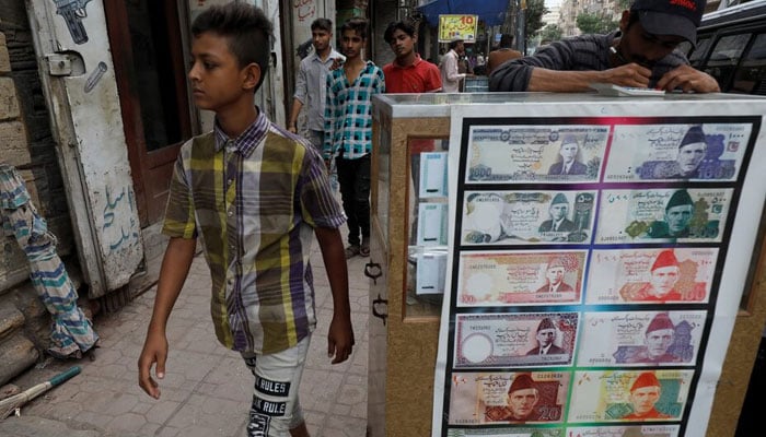 Boy walks past a sidewalk money exchange stall decorated with pictures of banknotes in Karachi. — Reuters/File