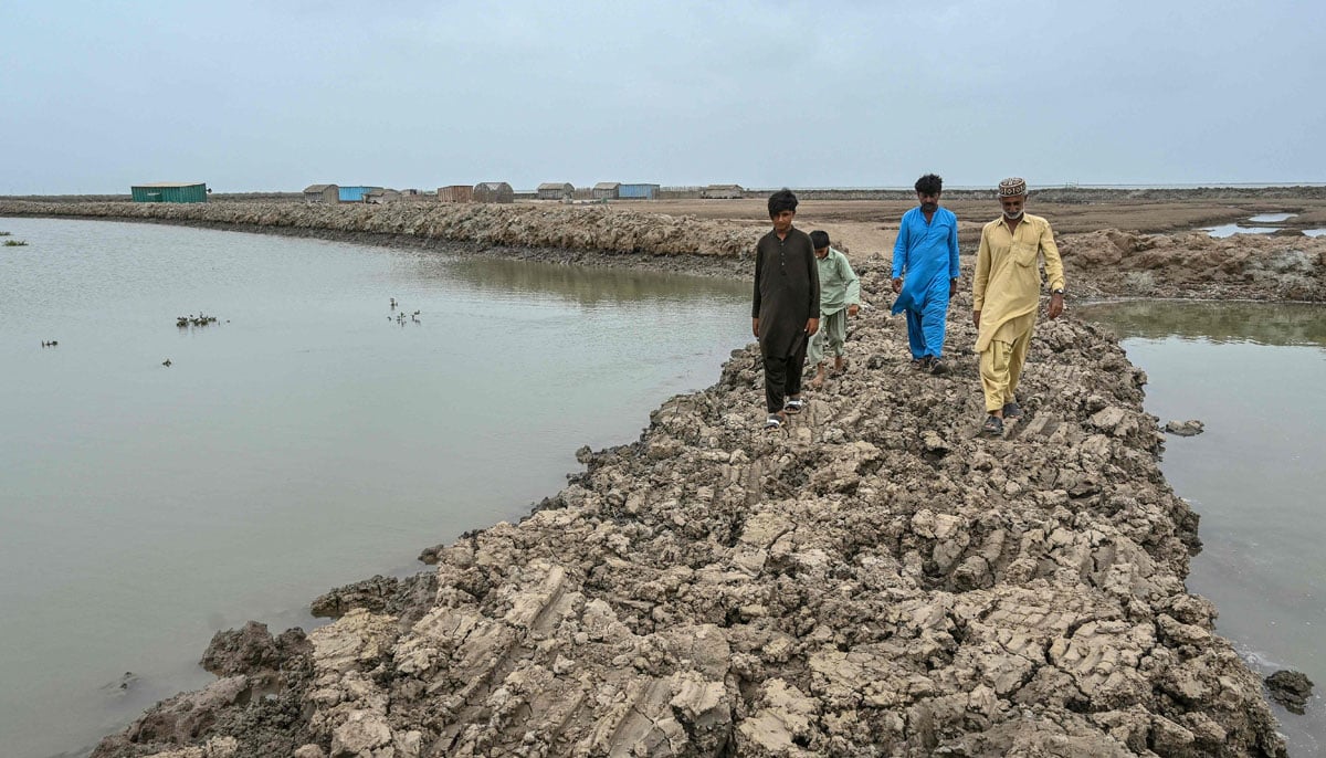 Fisherman Haji Karam Jat (right) walks along an embankment in Keti Bandar town of Thatta district near the Indus delta on June 25, 2025. — AFP