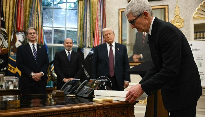 Apple CEO Tim Cook displays a memento on the Resolute Desk in the Oval Office of the White House in Washington, DC, on August 6, 2025 as US President Donald Trump (2nd R), Commerce Secretary Howard Lutnick (2nd L) and Treasury Secretary Scott Bessent (L) look on. — AFP