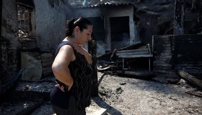 A woman walks inside the burnt tavern that she was working at, following a wildfire in Kaminia, near Patras, Greece, August 13, 2025. — Reuters