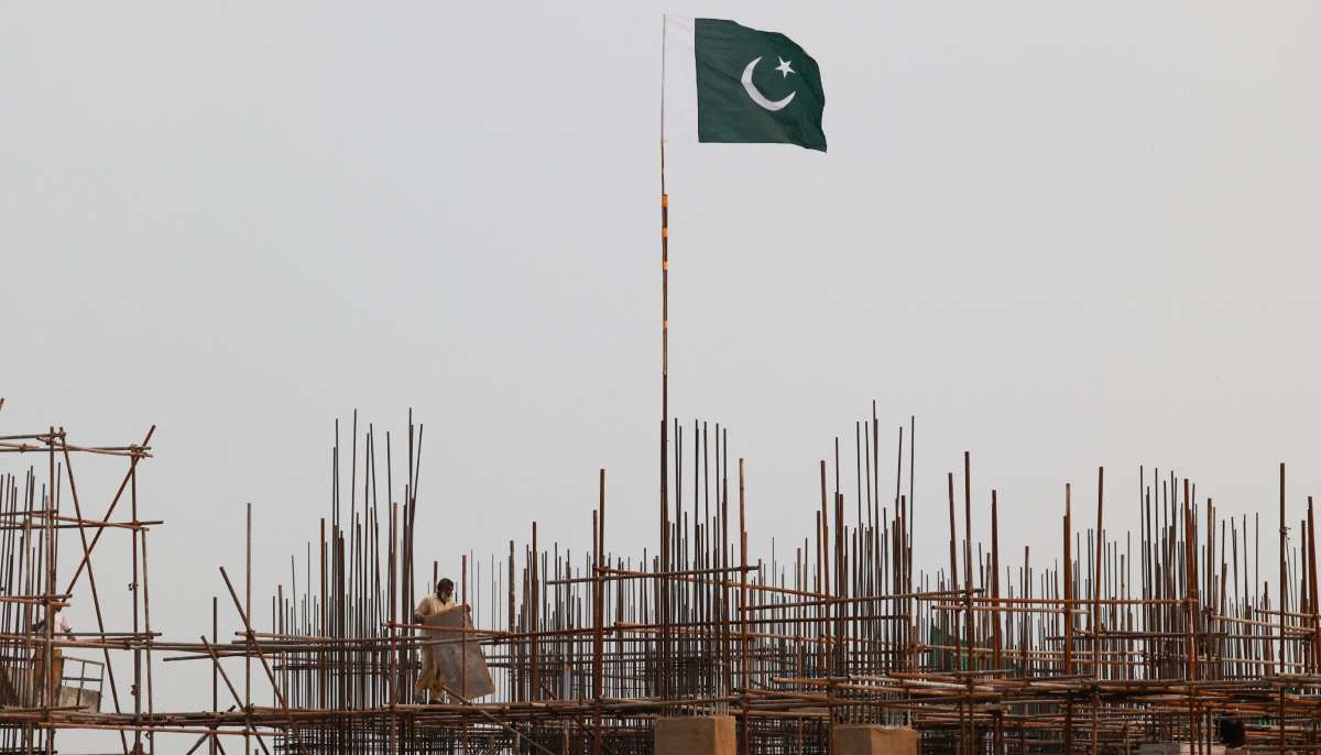 A Pakistani flag flutters over iron scaffoldings as a labourer works at a construction site on the eve of Pakistans Independence Day celebrations, in Lahore on August 13, 2025. — Reuters