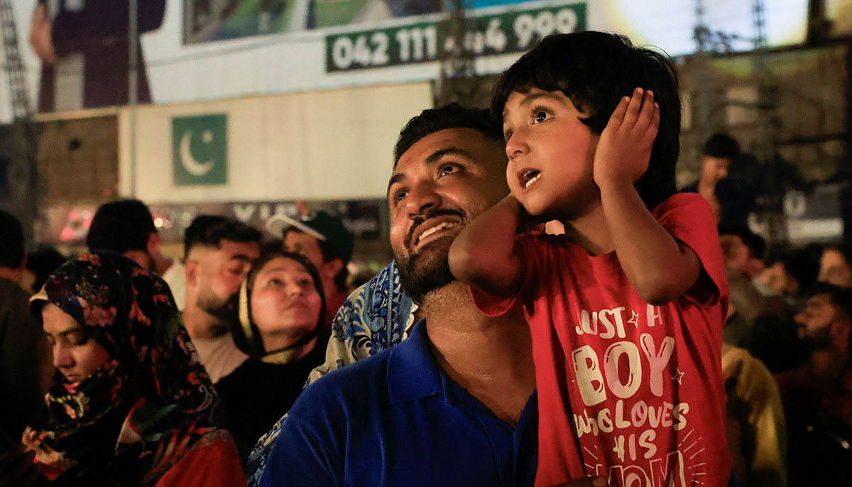A child covers his ears as he watches fireworks with his father during Independence Day celebration in Lahore on August 14, 2025. — Reuters