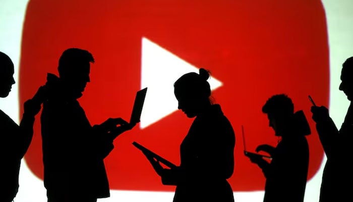 Silhouettes of laptop and mobile device users are seen next to a screen projection of Youtube logo in this picture illustration taken March 28, 2018. — Reuters