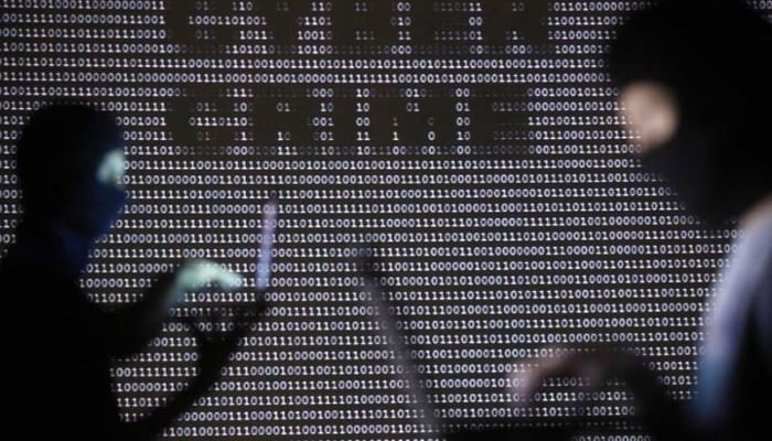 Representational image of people wearing balaclavas are silhouetted as they pose with a laptops in front of a screen projected with the word cyber crime and binary code. — Reuters/File