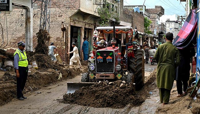 A tractor removes debris from a muddy road, after flash floods hit Buner, Khyber Pakhtunkhwa, on August 18, 2025. — AFP