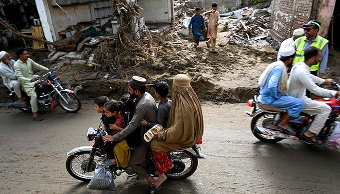 Commuters ride through a muddy road, after flash floods hit Buner, Khyber Pakhtunkhwa on August 18, 2025. — AFP