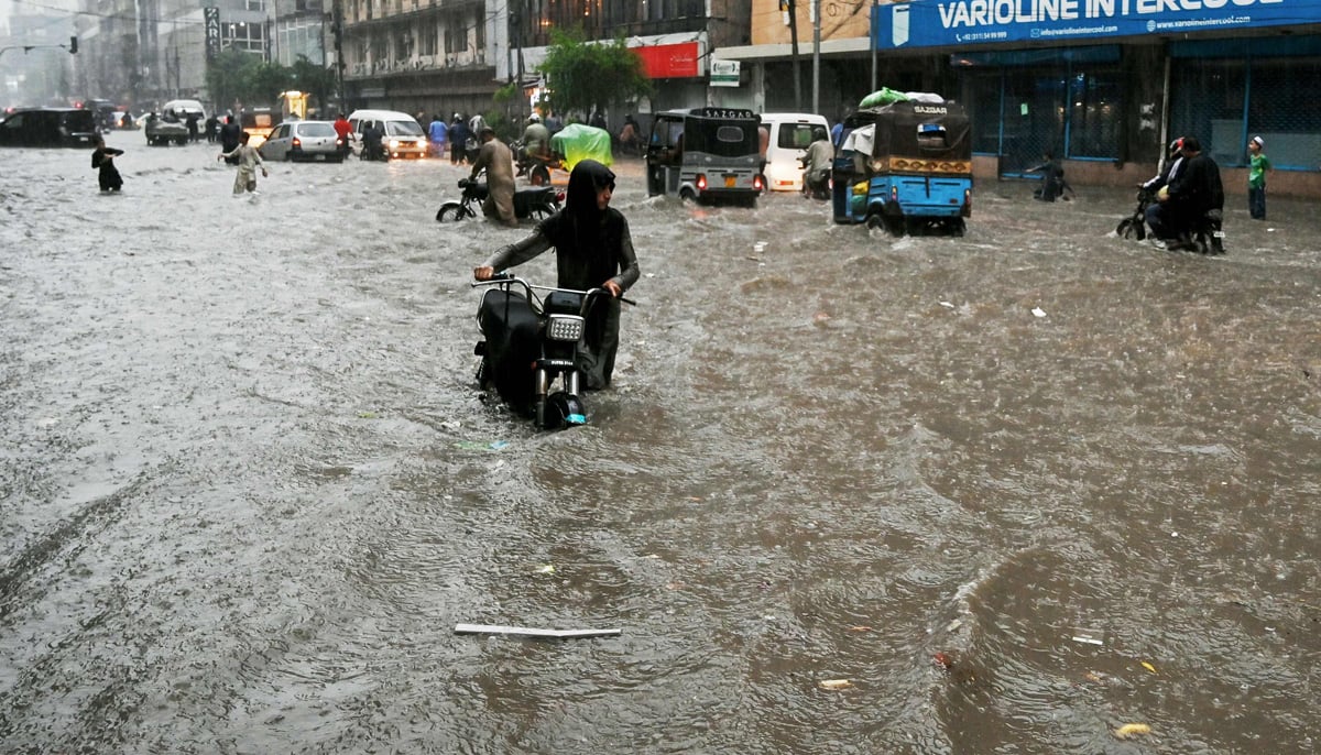 Commuters wade through a flooded street after heavy rainfall in Karachi on August 19, 2025. — AFP