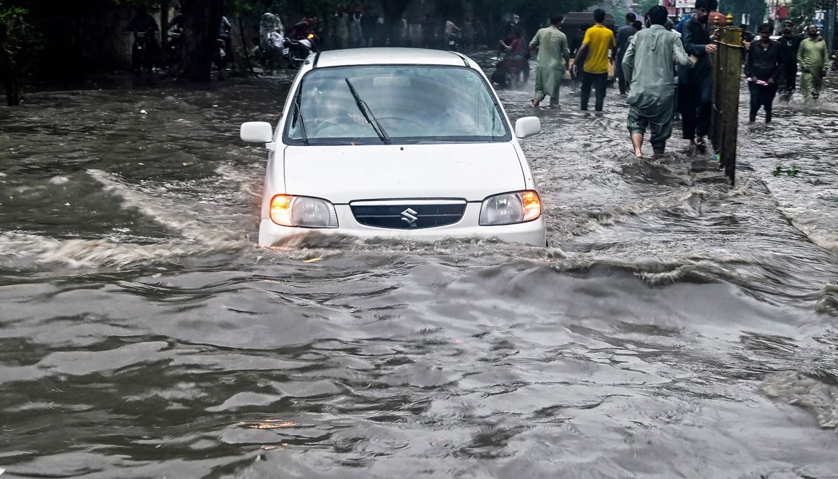 People wade through a flooded street after heavy rainfall in Karachi on August 19, 2025.