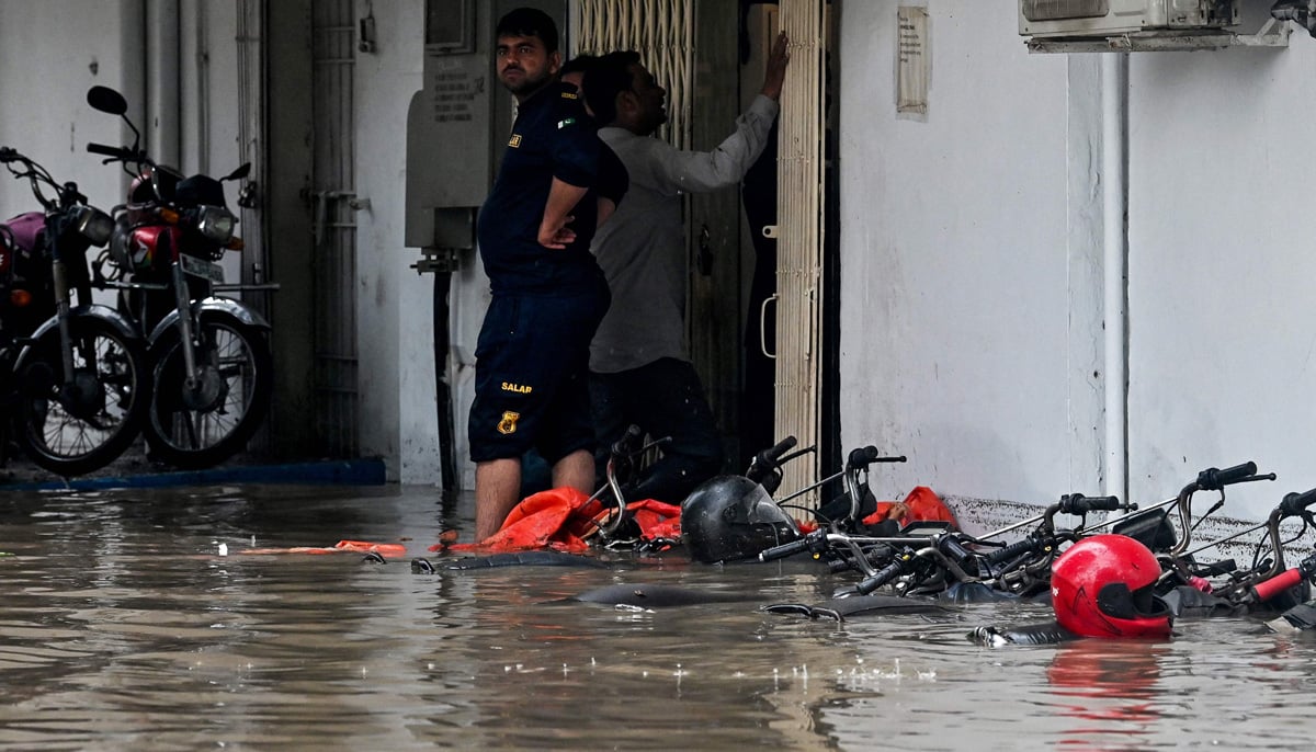 Men stand near motorbikes partially submerged in floodwaters along a street after heavy rainfall in Karachi on August 19, 2025. — AFP