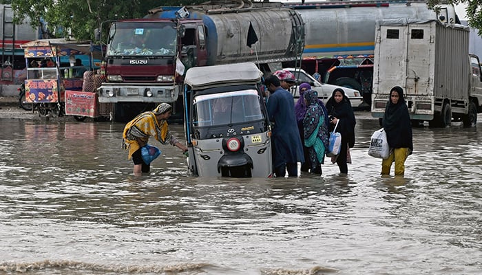 Passengers disembark from an auto rickshaw that got stranded on a flooded road after heavy monsoon rains in Karachi on August 20, 2025. — AFP