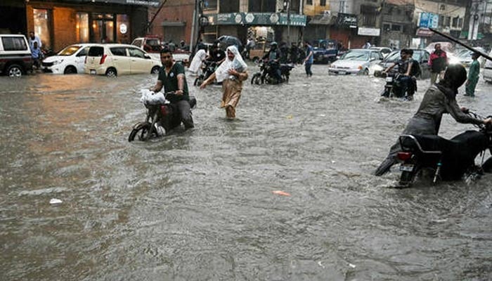 People wade through a flooded street after heavy rainfall in Karachi on August 19, 2025. — AFP