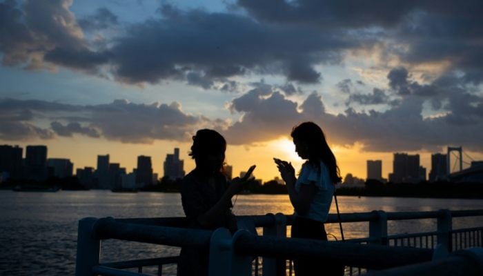 Two women using their smartphones in Japan. — AFP