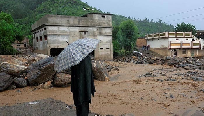 A resident stands with an umbrela as rain water flowing from mountains crosses a damaged area, following a storm that caused heavy rains and flooding in Buner district, Khyber Pakhtunkhwa on Aug 18, 2025. — Reuters