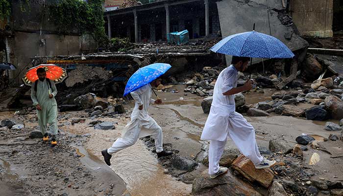 Volunteers walk with umbrellas to avoid rain as they survey the damaged areas, following a storm that caused heavy rains and flooding in Bayshonai Kalay, in KPs Buner district on August 18, 2025. — Reuters