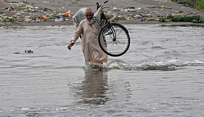 A man carries his bicycle as he wades along a flooded road after heavy monsoon rains in Karachi on August 20, 2025. — AFP