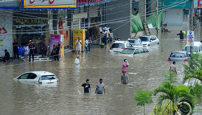 People wade through a flooded road with partially submerged vehicles after the monsoon rain, in Karachi, August 19, 2025. — Reuters
