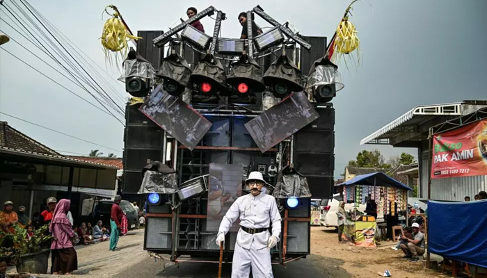 A man dressed as a character stands in front of a truck mounted with a tower of subwoofers used at Independence Day celebrations in Malang, East Java. — AFP