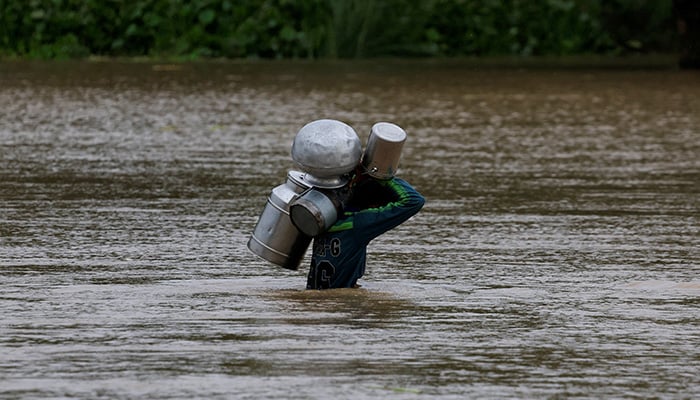 A resident carries milk buckets as he crosses a flooded road, due to the monsoon rains and rising water level of the Sutlej River, in Bhikhiwind village, near the Pakistan-India border in Kasur district of the Punjab, August 24, 2025. — Reuters