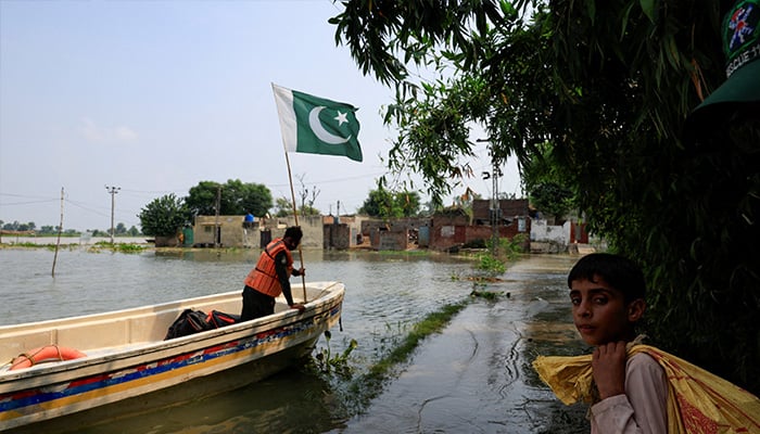 A resident carries a sack of supplies as a volunteer of Rescue 1122 adjusts Pakistans flag on a boat, which was used to evacuate people from the areas flooded due to the monsoon rains and rising water level of the Sutlej River, in Bhikhiwind village near the Pakistan-India border in Kasur district of the Punjab, August 23, 2025. — Reuters
