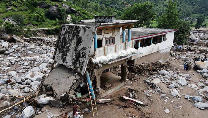 An aerial view shows flood survivors standing near a damaged house surrounded by heavy rocks in the Buner district of mountainous Khyber Pakhtunkhwa on August 17, 2025. — AFP