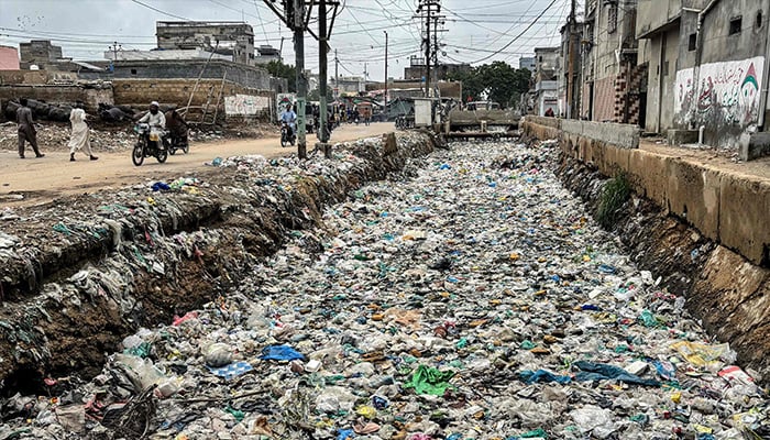 People ride past a drain clogged with plastic waste, disposed along a roadside in Karachi on August 24, 2025. — AFP