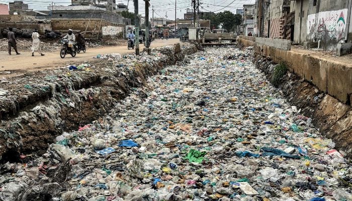 People ride past a drain clogged with plastic waste, disposed along a roadside in Karachi on August 24, 2025. — AFP