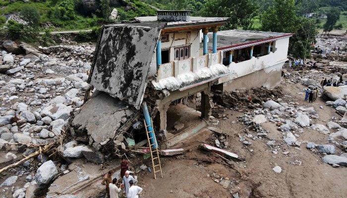 An aerial view shows flood survivors standing near a damaged house surrounded by heavy rocks in the Buner district of mountainous KP on August 17, 2025. — AFP