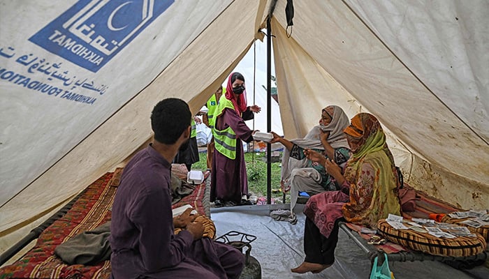 A volunteer (C) distributes food to flood-affected people at a makeshift camp in Chung, in Punjab province, on August 31, 2025. — AFP