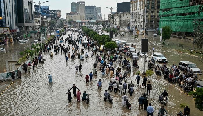 People wade through a flooded street after heavy rainfall in Karachi on August 19, 2025. — AFP