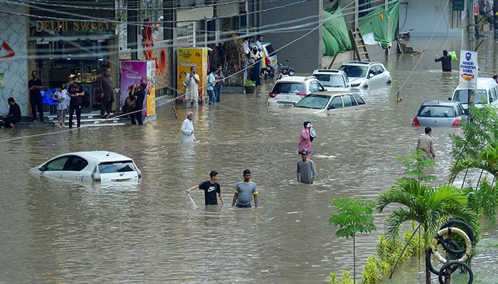 People wade through a flooded road with partially submerged vehicles after the monsoon rain, in Karachi, August 19, 2025. — Reuters