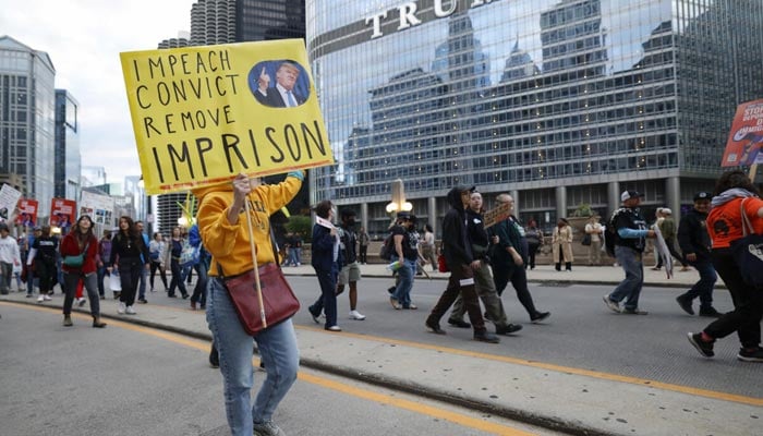 People hold anti-Trump signs as they march past Trump International Hotel & Tower in Chicago during a demonstration against the planned deployment of National Guard troops. — AFP