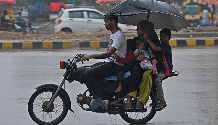 A family rides a motorcycle along a street during rainfall in Karachi on September 9, 2025. — AFP