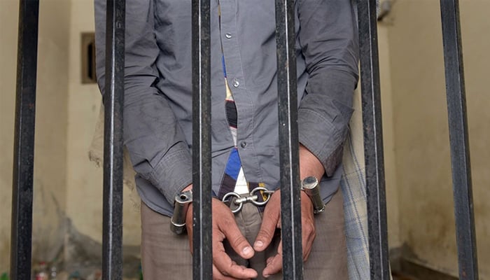 Representational image of a handcuffed man standing behind the bars