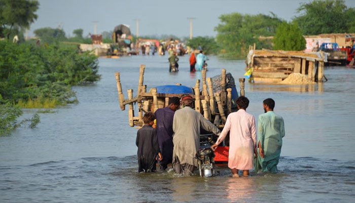 Men walk along a flooded road with their belongings, following rains and floods during the monsoon season in Sohbatpur August 28, 2022. — Reuters