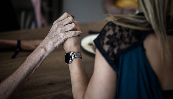 This picture taken on September 9, 2020 shows a volunteer (R) holding the hand of an Alzheimers patients during lunch at the restaurant of the village Landais Alzheimer site for Alzheimers patients in Dax, southwestern France. — AFP