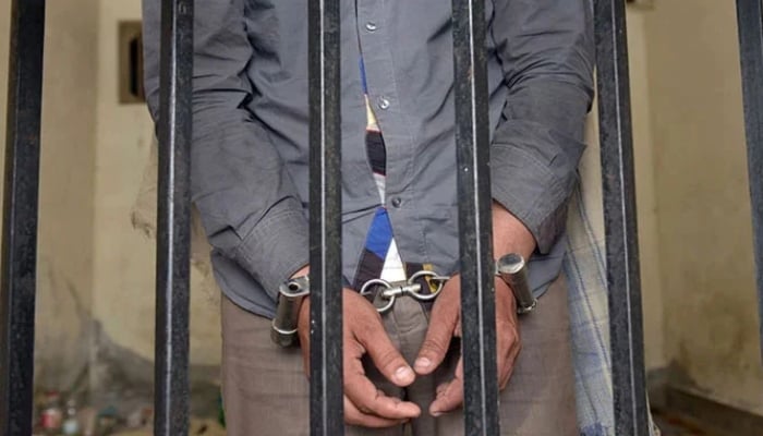 The picture shows a person handcuffed and standing behind bars. — AFP/File