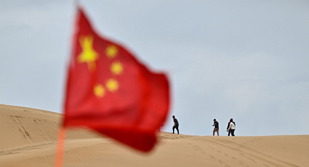 This picture taken on August 12, 2025 shows people visiting a tourist area in the Kubuqi desert near Ordos, in China´s northern Inner Mongolia region, as the China national flag is seen in the foreground. — AFP