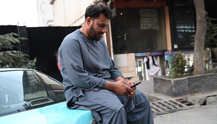 An Afghan taxi driver uses his mobile phone as he sits on his vehicle along a street in Kabul on October 1, 2025. — AFP