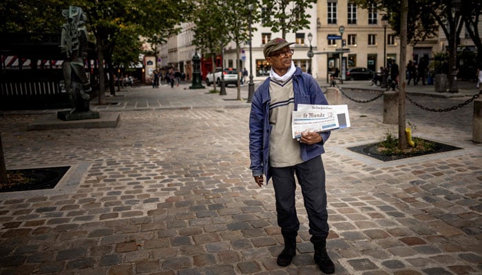 Pakistani born 73-year-old newspaper hawker Ali Akbar poses as he sells newspaper copies in the street.— AFP