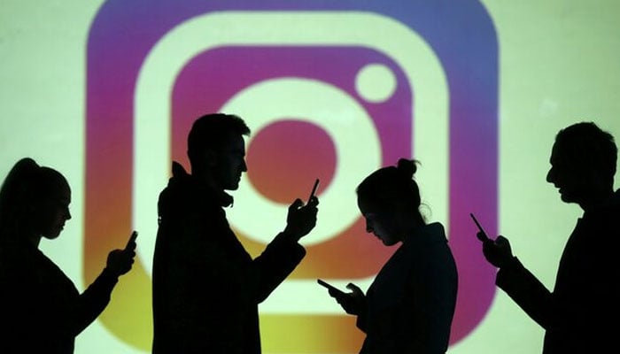 Silhouettes of mobile users are seen next to a screen projection of Instagram logo in this picture illustration taken March 28, 2018.— Reuters