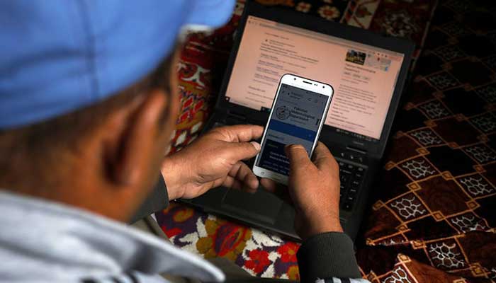A man monitors a metrological website on his mobile phone and laptop, at home in Hassanabad village. — Reuters/File